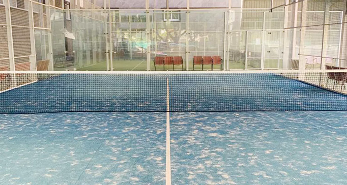 Pista de pádel cubierta con césped azul y muros de cristal