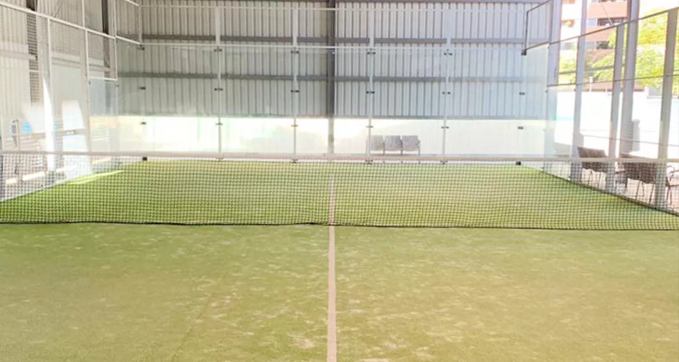Pista de pádel cubierta con césped verde, muros de cristal y estructura metálica